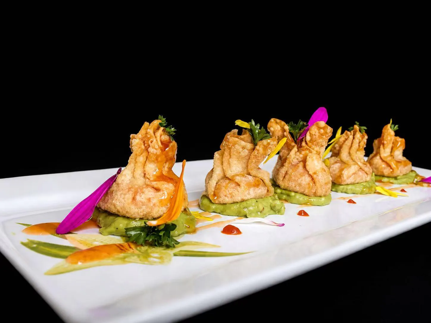 Crispy fried wonton appetizers arranged on green sauce with edible flowers at Wasu Sushi Ramen, a Sushi restaurant in Bedminster